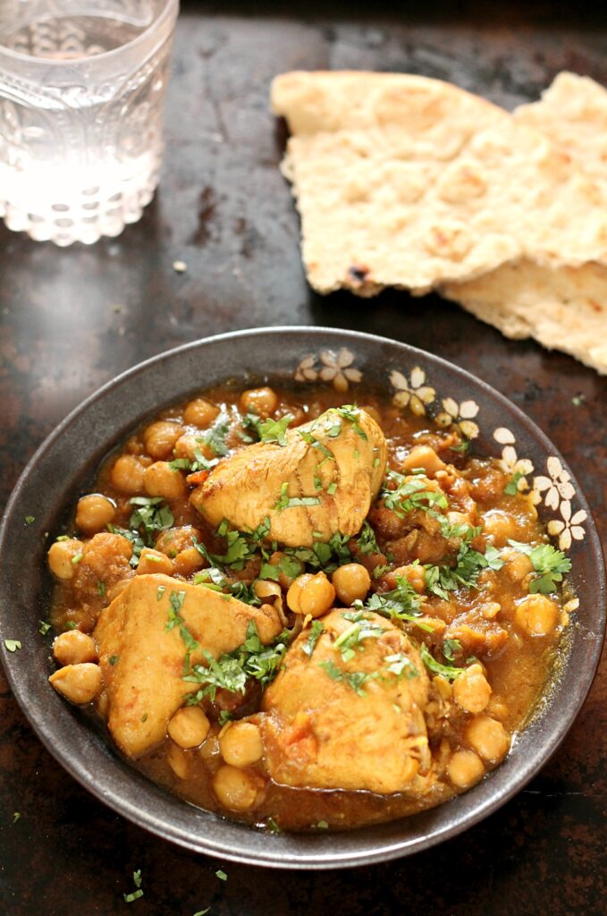 Murgh Cholay in a black bowl garnished with cilantro with naan in the background.