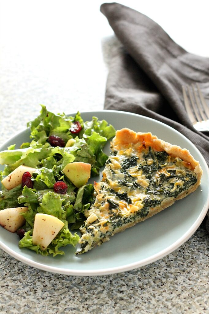 A slice of Kale and Leef Quiche on a blue plate with salad on the side.
