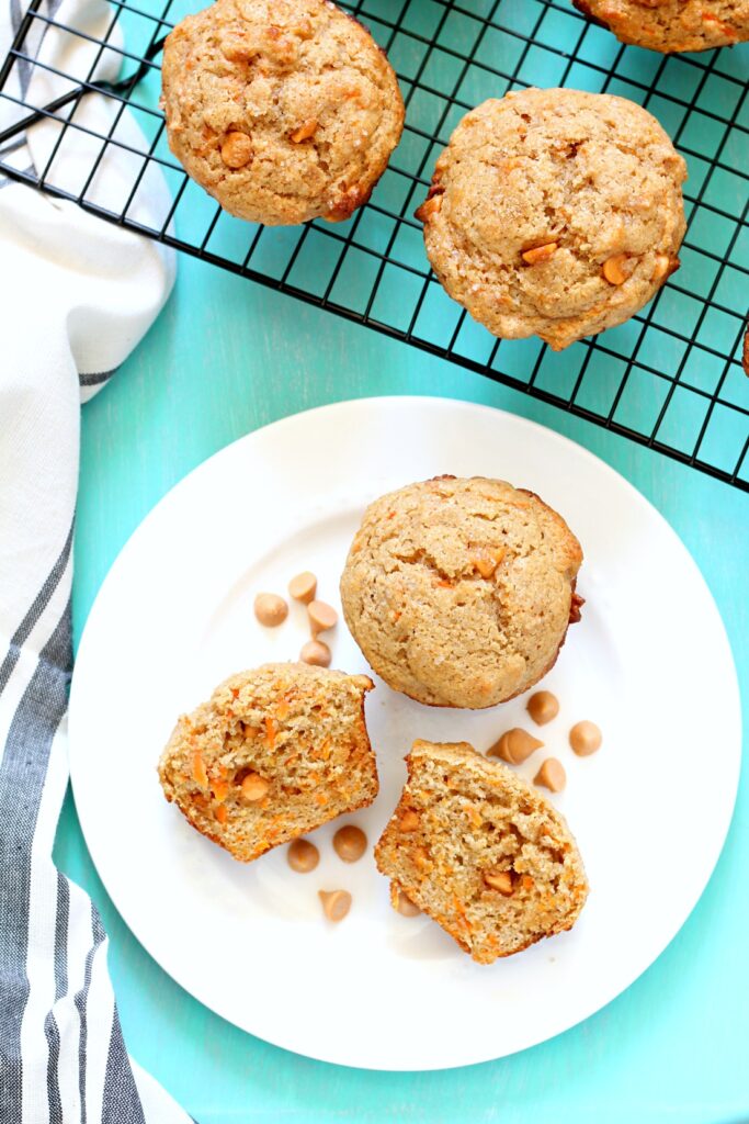 Two whole wheat butterscotch chip muffins on a white plate where one is cut in half.