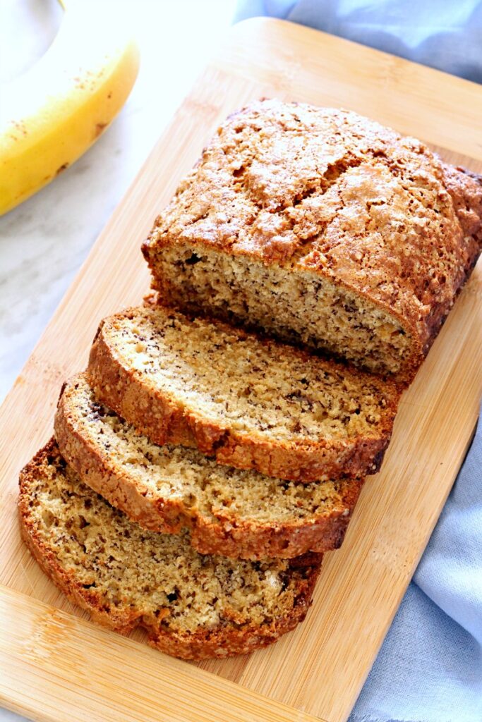 Banana Bread Loaf partially sliced on a wooden cutting board.