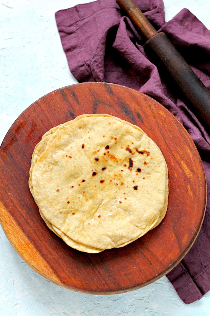 A stack of rotis on a round wooden cutting board.