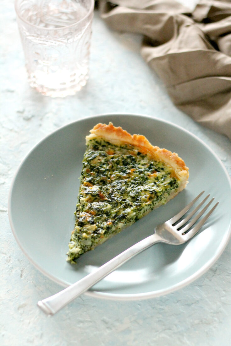 A slice of Spinach Quiche on a blue plate with a silver fork.